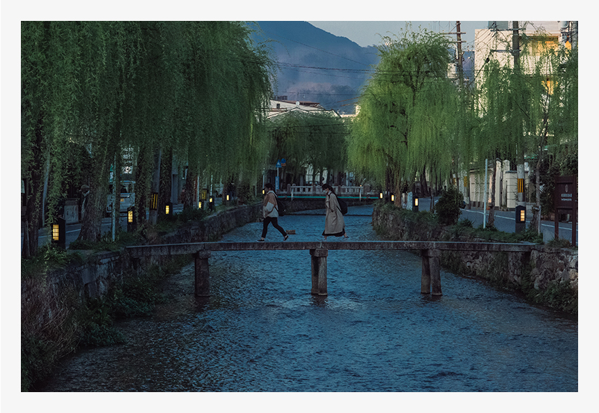 夕暮れの京都、白川の風景。両岸の明かりが美しい。手前から奥までピントを合わせるために絞りはF11に。川の流れをぶらさず撮影するためにISO感度を10000に上げて、速めのシャッタースピード（1/2000秒）で撮影。